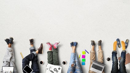 Mehrere junge Menschen strecken entspannt die Beine aus während ihre Arbeitsmaterialien neben ihnen liegen