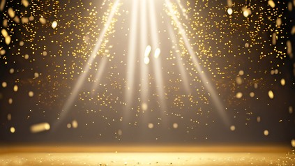 Goldenes Konfetti regnet auf eine Bühne, die von einem Scheinwerfer beleuchtet wird.