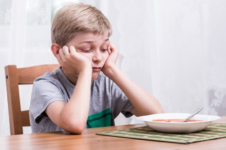 Kind sitzt enttäuscht vor seiner Suppe