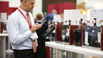 Ein Mann fotografiert mit seinem Smartphone eine Flasche Wein auf einer Messe