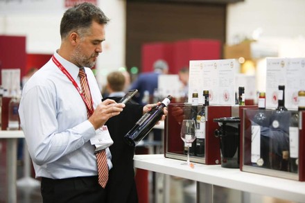 Ein Mann fotografiert mit seinem Smartphone eine Flasche Wein auf einer Messe