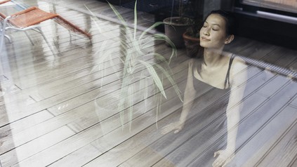 Frau, die am Fenster steht und tief einatmet