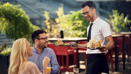 Kellner bringt Speisen zu Restaurantgästen, die im Außenbereich sitzen