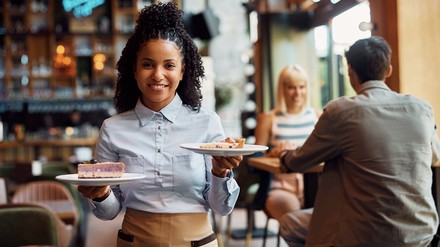 Junge Kellnerin arbeitet mit Freude im Service. (Foto: © Drazen/stock.adobe.com)