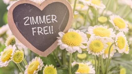 Ein herzförmiges Schild auf dem Zimmer Frei! steht steht in einer Blumenwiese