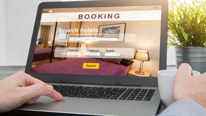 Ein Mann sitzt vor einem Laptop auf dem eine Hotelbuchungsseite geöffnet ist