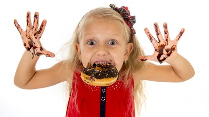 Kind mit Schokolade an den Fingern und Donut im Mund