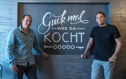 Hernando Ospina und Daniele Marino stehen vor einem Schild auf dem Guck mal wer da kocht steht