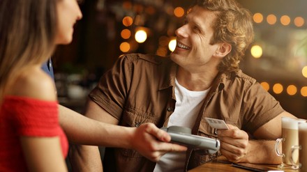 Junger Mann bezahlt bargeldlos in einem Restaurant, lächelnd, gute Stimmung