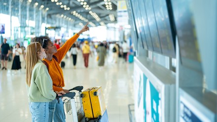 Zwei Frauen am Flughafen schauen auf die Anzeigetafel.