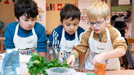Drei Kitakinder schmecken gemeinsam bei einer Kochaktion ab.