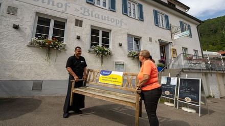 Die Wirtsleute Raul Yigit und Andrea Schneider-Yigit vom Gasthof Blautopf positionieren vor ihrem Lokal eine Bank, auf der sie fordern, dass man das Naturdenkmal Blautopf jederzeit besichtigen können muss.