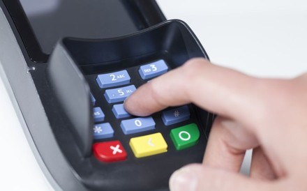 Eine Hand tippt auf einem Kartenzahlgerät eine Geheimzahl ein