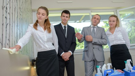 Drei Azubis lernen mit ihrem Ausbilder in einem Hotelzimmer