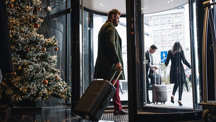 Pärchen verlässt ein Hotel mit Weihnachtsbaum durch die Drehtür