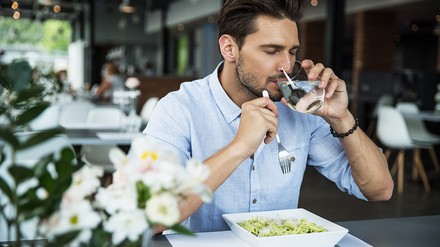 Mann der in einem Restaurant aus einem Glas Wasser trinkt