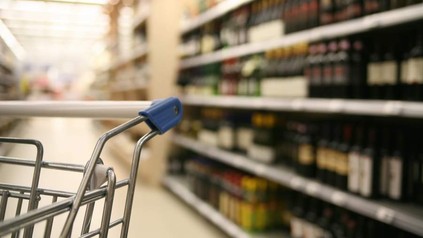 Ein leerer Einkaufswagen vor einem Alkoholregal im Supermarkt