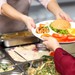 Frau gibt einer Schülerin in der Mensa Mittagessen aus.