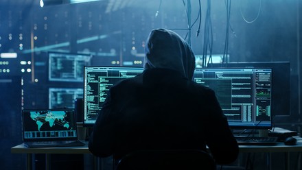 Ein Hacker sitz vor Computerbildschirmen.