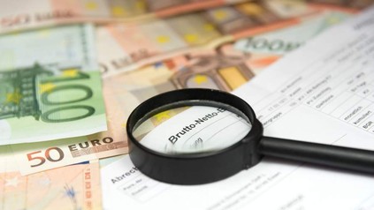 Eine Abrechnung und eine Lupe liegen auf mehreren Geldscheinen