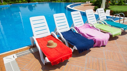 vor einem Pool stehen fünf Liegen, die alle mit bunten Handtüchern belegt sind