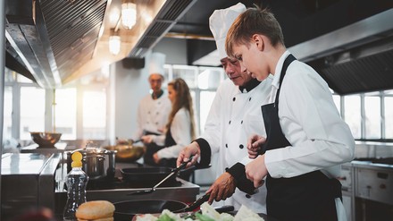 Auszubildender Koch bekommt Hilfe von einem älteren Koch