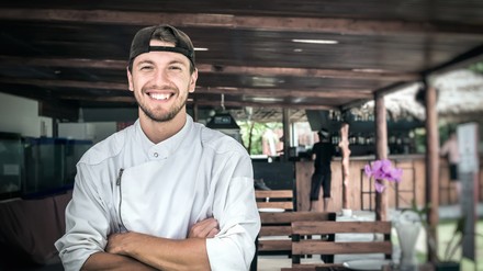 Junger Koch steht mit verschränkten Armen da und lacht