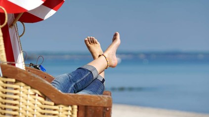 Eine Frau liegt entspannt in einem Strandkorb und legt die Füße hoch