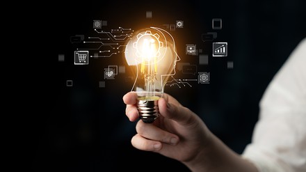 Glühbirne wird hochgehalten, darauf verschiedene Symbole rund um das Thema KI