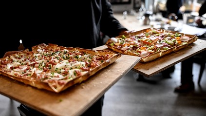 Servicekraft hält zwei Bretter mit Flammkuchen