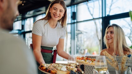 Servicekraft bringt Speisen an den Tisch