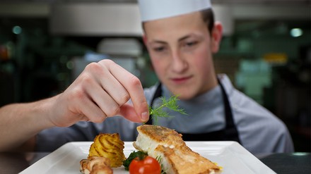 Junger Koch garniert Gericht auf Teller