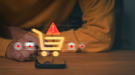 Smartphone mit eingeblendeten Warnsymbolen und Einkaufswagen-Icon – Symbolbild für manipulative Designs und strengere Regeln beim Online-Vertragsabschluss.