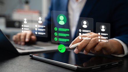 Person am Laptop nutzt ein digitales Recruiting-Interface; mehrere Bewerberprofile werden angezeigt, eines ist markiert und mit Häkchen bewertet.