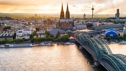 Panorama von Köln bei Sonnenuntergang mit Kölner Dom, Hohenzollernbrücke und Rhein im Vordergrund.