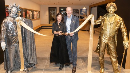 Birgit Maier und Alexander Strobl schneiden beim Opening der „World of Congress“ im Hotel Gut Brandlhof ein Band durch; daneben stehen zwei Künstler als goldene Statuen.