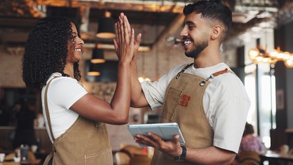 Zwei Servicekräfte im Restaurant geben sich ein High Five, eine Person hält ein Tablet in der Hand.