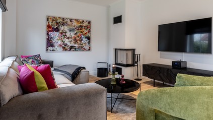 Moderner Wohnraum eines Landhaus-Stricker-Appartements auf Sylt mit Sofa, Kamin, Kunstwerk und großzügiger Einrichtung