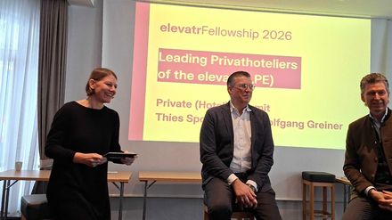 Moderation und zwei Speaker auf Stühlen vor einer Präsentationsfolie „Leading Privathoteliers“ beim elevatrFellowship 2026.