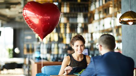 Junges Paar sitzt an einem Restauranttisch und genießt gemeinsam ein Essen zum Valentinstag.