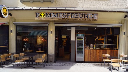 Pommes Freunde Filiale von außen mit Biertischen und Bierbänken