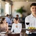 Junger Kellner im Restaurant präsentiert Salat und Wein auf einem Tablett – Symbolbild für junge Beschäftigte im Gastgewerbe und die Generation Z.