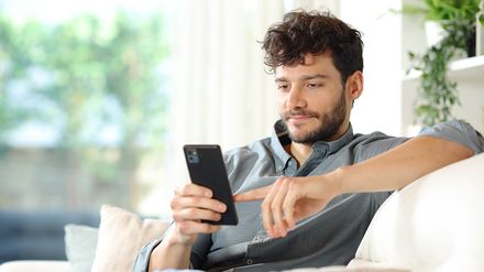 Mann sitzt auf einer Couch und schaut auf sein Smartphone