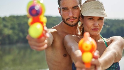 Ein Pärchen in Badekleidung zielt mit Wasserpistolen