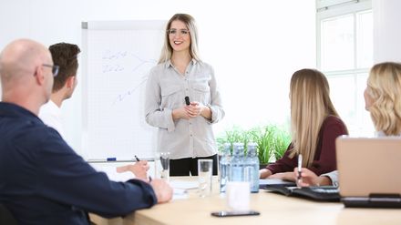 Junge Frau hält eine Schulung vor einer Gruppe von Mitarbeitern in einem Seminarraum.