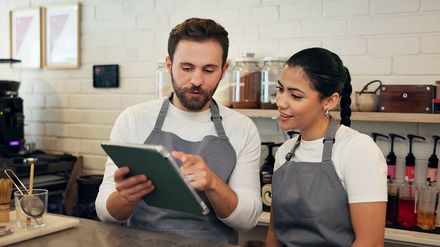 Mitarbeiter in einem Café besprechen am Tablet digitale Bestellungen, Bewertungen und Abläufe