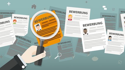 Hand hält Lupe über mehrere Bewerbungsunterlagen mit Lebensläufen