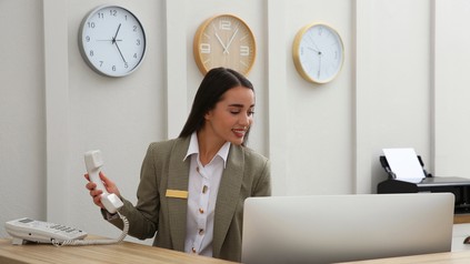 Rezeptionistin mit Telefonhörer in der Hand schaut auf ihren Computer