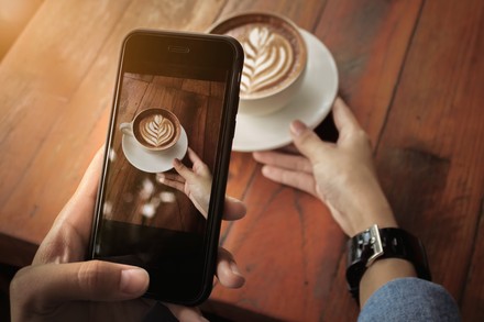 Frau fotografiert Cappuccino mit Smartphone