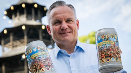 Christian Scharpf hält zwei offizielle Wirtekrüge für das Oktoberfest 2026 vor dem Chinesischen Turm in München
